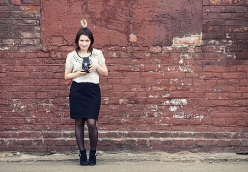 Woman photographer holding retro camera and taking photo on vintage brick wall background. Toned photo with copy space. Vintage style photo.