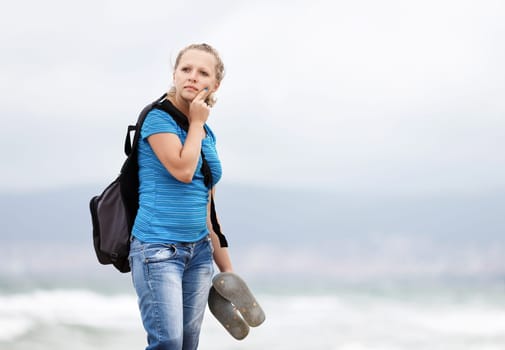 Pretty young blonde woman with a backpack standing outdoors. Girl with backpack. Selective focus on model.