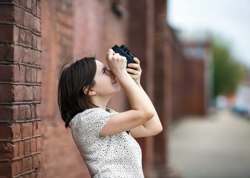 Photographer woman girl is holding old vintage camera and taking photographs. Photo in retro style. Shallow depth of field. Selective focus on model.