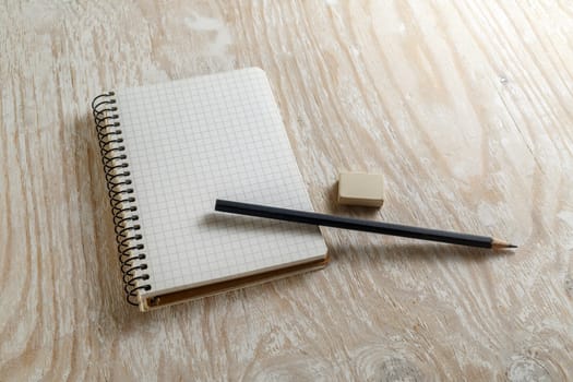 Notepad with a pencil and eraser on a light wooden background.