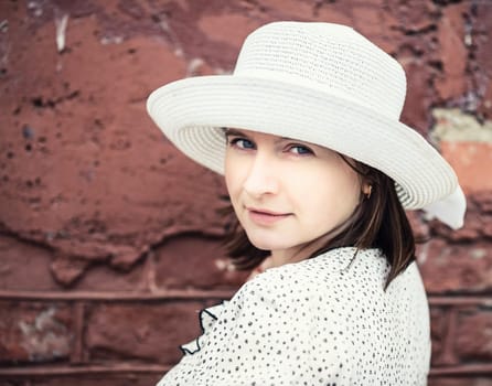 Pretty young woman in white hat against brick wall background. Close-up female portrait. Close-up vintage portrait of a woman. Selective focus. Vintage style photo.