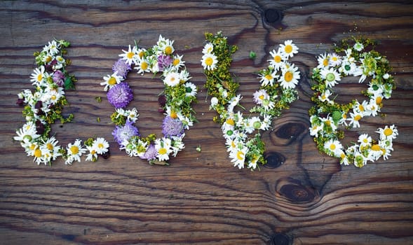 Inscription LOVE made of flowers and leaves on vintage wooden table background. Word love made of flowers.Top view.