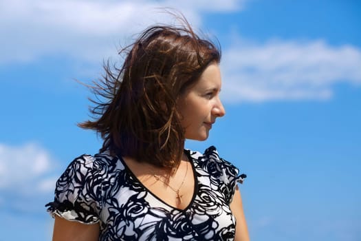 A beautiful young woman with hair flying in the wind against the blue sky. Female profile close-up.