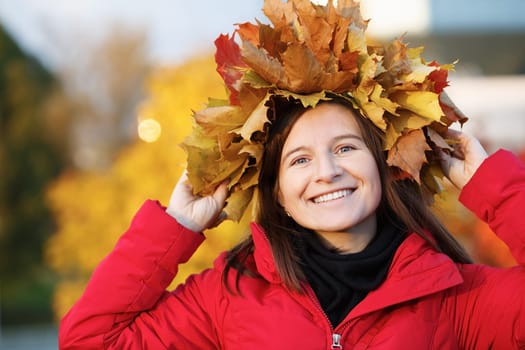 Happy young woman with wreath of maple leaves. Autumn female portrait. Selective focus on model.