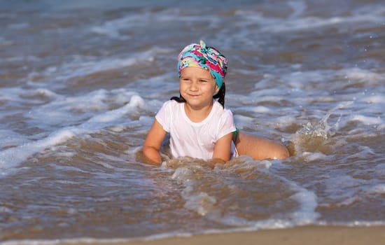 Happy child in a white t-shirt and colorful bandana having fun in the water at the beach.