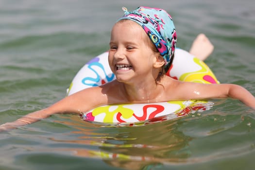 Laughing baby bathing in the sea and floats on inflatable ring. Shallow depth of field. Focus on the model's face.