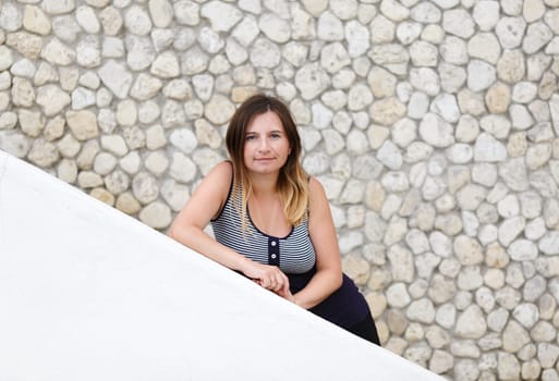 Pretty young woman posing, leaning on the parapet on the background of stone vintage wall. Selective focus on model.