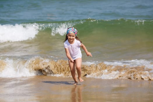 Child runs along the beach on a background of a sea wave. Shallow depth of field. Focus on model.