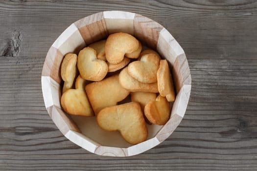 Heart shaped cookies in a wooden container on wooden background. Top view.