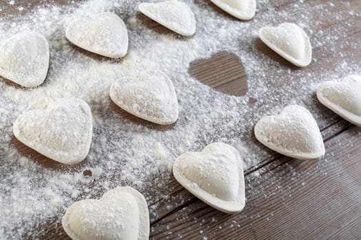 Cooking ravioli. Raw dumplings in the form of hearts sprinkled flour on wooden background closeup. Shallow depth of field.