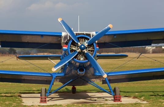 Blue single-engine biplane in retro style. Old airplane. Frontal view of the propeller engine and cockpit.