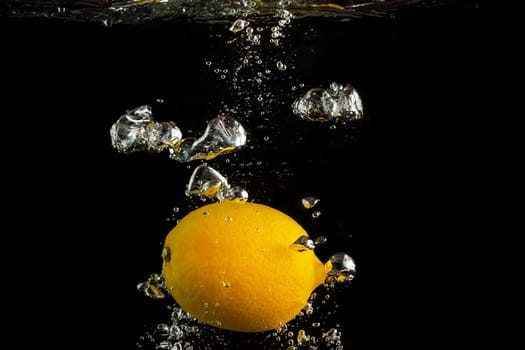 Fresh lemon falling into the water with a splash and air bubbles. Yellow lemon in water on black background. Healthy food. Wash fruits.