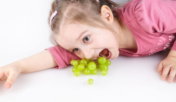 Baby girl lying down and eating green grapes. Studio shot.