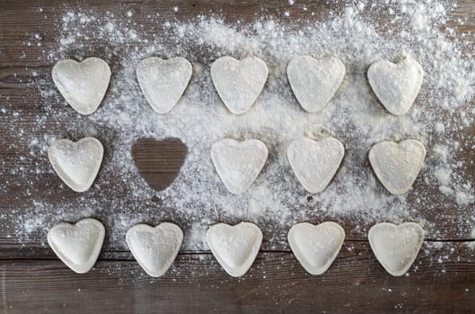 Heart shaped ravioli sprinkle with flour, on wooden background. Uncooked ravioli hearts. Cooking dumplings. Top view.