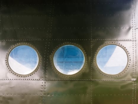 Portholes on military green painted metal background with rivet. Three portholes on board old retro airplane. Outside view of the old aircraft.