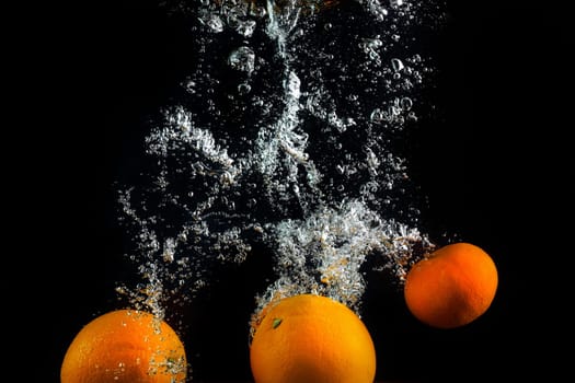 Fresh oranges and tangerines splash in water with air bubbles. Oranges in water on a black background. Healthy food. Wash fruits.