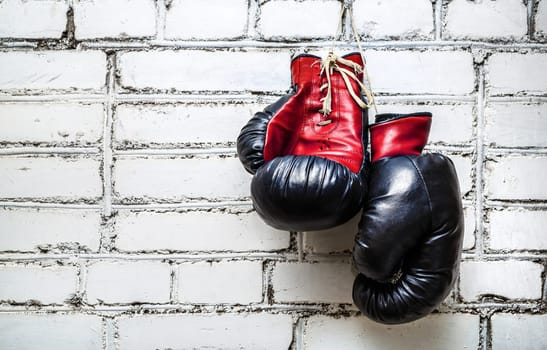 Pair of old red boxing gloves hanging on white brick wall.