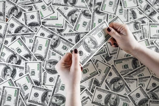 Check the authenticity of money. One hundred dollar bill in female hands on a background of money. Checking money. Cash in hands. Fake money in hands. Money in female hands.