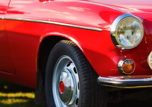 Red vintage car. Close-up fragment of the red vintage car. Headlight of vintage red car. Retro car. Selective focus.