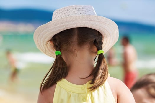 A child in a white hat admiring sea views. View from the back. Blurred background bokeh. Shallow depth of field. Selective focus.