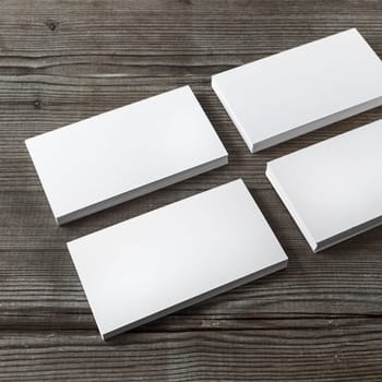 Set of blank white business cards on a dark wooden background. Template for branding identity. Shallow depth of field.
