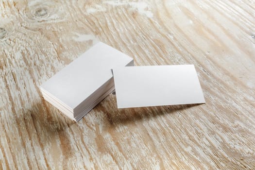 Blank business cards with soft shadows on light wooden background. Template for design presentations and portfolios. Studio shot.