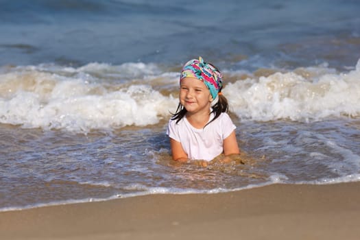 Smiling child in a white t-shirt lying in water on the beach. Shallow depth of field. Focus on the model's face.