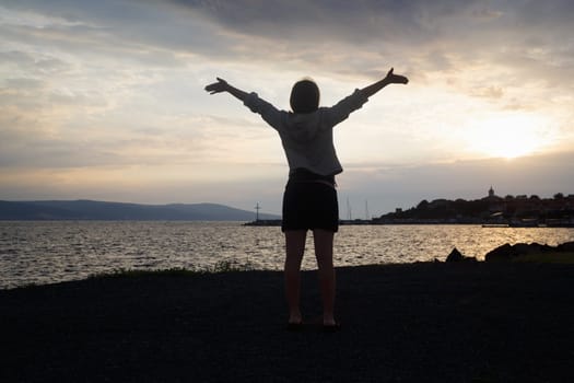 Silhouette of a girl with raised hands on the background of sunrise over the sea. Focus on model. Shallow depth of field