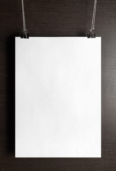 Blank white paper poster hanging on a wooden background. Vertical shot.