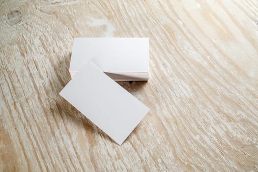 Photo of blank business cards with soft shadows on light wooden textured background. For design presentations and portfolios.