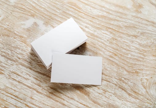 Blank business cards with soft shadows on light wooden background. Template for design presentations and portfolios. Studio shot.