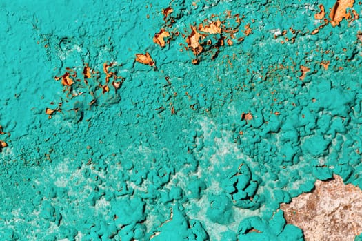 A fragment of the old wall, painted bright turquoise paint, cracked over time. Peeling paint texture.
