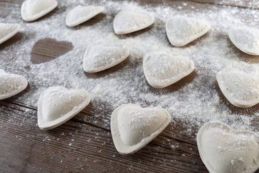 Raw ravioli in the shape of hearts, sprinkle with flour, on dark wooden background. Cooking dumplings. Shallow depth of field.