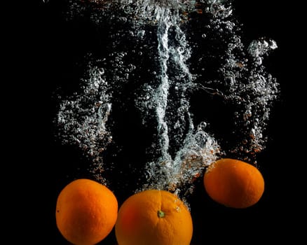 Oranges fall in the water with air bubbles. Photo on black background.