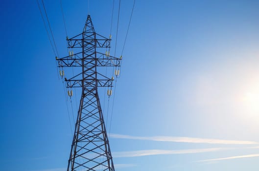 Electricity pylon silhouetted against blue sky background. High voltage tower.