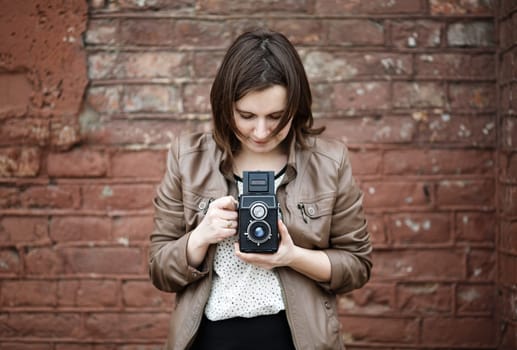 Girl with vintage camera taking photo on brick wall background. Selective focus on camera.
