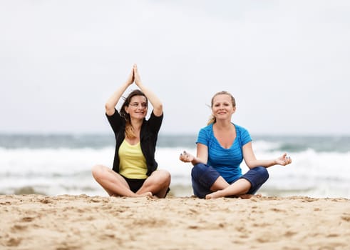 Two smiling young women sitting and relax in lotus pose outdoors. Two happy girls sitting outdoors. Selective focus on the models.