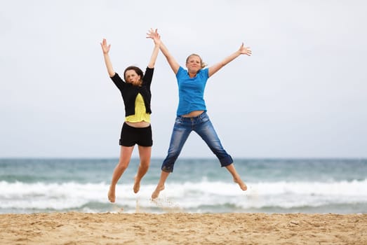 Two happy girls jumping on the beach against the sea and cloudless sky. Shallow depth of field. Focus on the model.