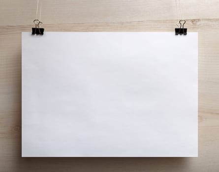 White paper poster hanging on light wooden background.
