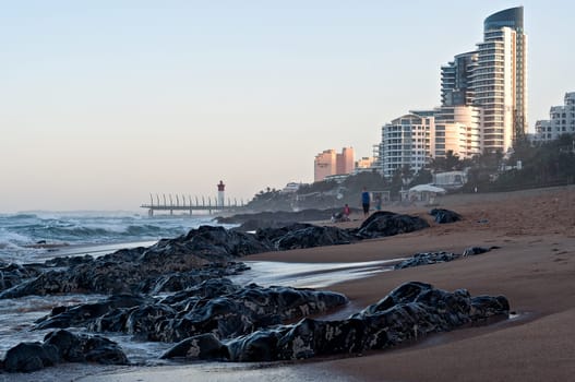 DURBAN, SOUTH AFRICA - JULY 11, 2016: People on the beach at Umhlanga Rocks, with the Millennium Pier and lighthouse in the background.