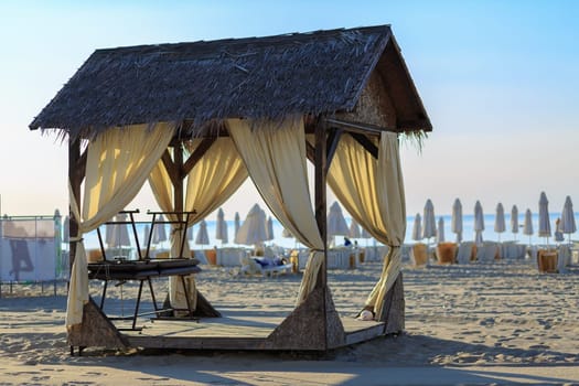 Massage canopy with thatched roof on the sandy beach. Early morning. Shallow depth of field. Selective focus.