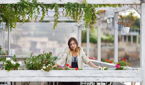 Portrait of a pretty young woman in a vintage setting. Framing of the pure white paint wooden structures with ivy and flowers. Shallow depth of field. Focus on foreground and model.