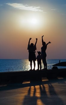 Two women and little girl greeted the dawn over the sea. Focus on models. Shallow depth of field. Toned image.