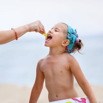 A child eats a grape on the beach. Mom's hand feeding baby. Baby eats.