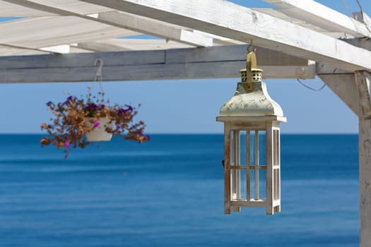 Painted white paint bleached wooden vintage lantern against the blue sky and sea. Shallow depth of field. Selective focus on the lantern.