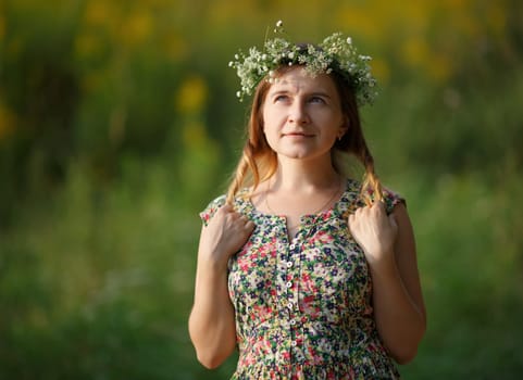 Young woman with wreath holding his hair and looking up. Sunset light. Shallow depth of field. Focus on model.