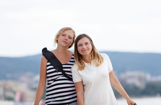 Two attractive young women outdoor. Mountains on blurred background. Shallow depth of field. Focus on models.