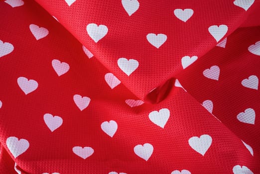 Pattern of white hearts on a bright red fabric with pleats. Top view.