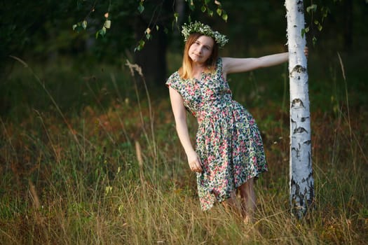 Girl with a wreath on his head keeps for birch. Sunset light. Shallow depth of field. Focus on model.