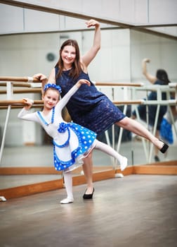 Mom and daughter posing at ballet barre. Happy family in a dance class. Mother and daughter practicing during class at a ballet school. Shallow depth of field. Selective focus.